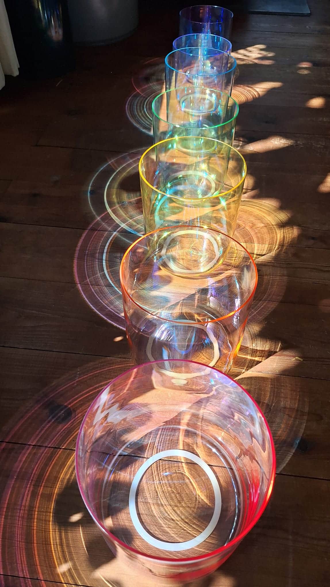 Kristallen klankschalen op een rij met kleurrijk lichtspel op de houten vloer